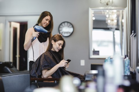 Stylist blow drying client's hair in salon