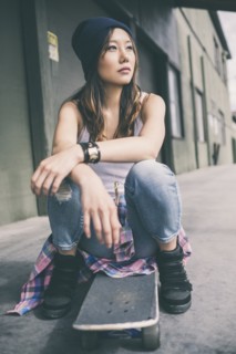 Korean woman sitting on skateboard on city street