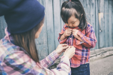 Korean mother helping daughter button her shirt
