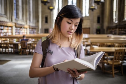 Chinese woman standing in library reading book