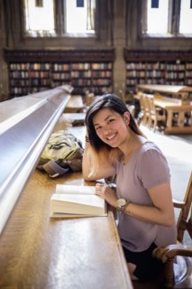 Smiling Chinese woman sitting in library reading book
