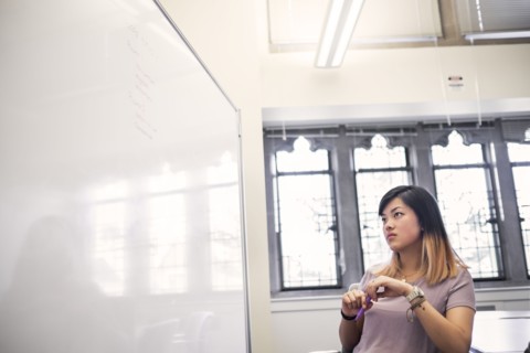 Chinese woman holding marker reading whiteboard