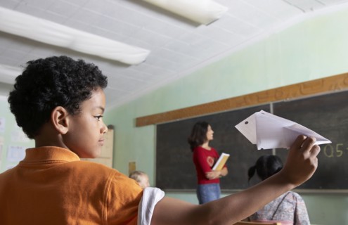 Mixed Race boy throwing paper airplane in class