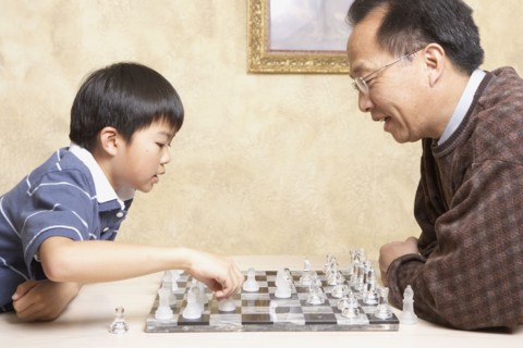 Asian father and young son playing chess