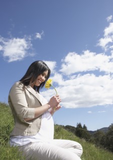 Pregnant Asian woman holding flower outdoors
