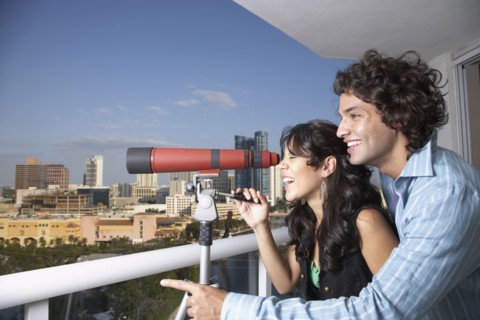 Hispanic couple looking through telescope on balcony