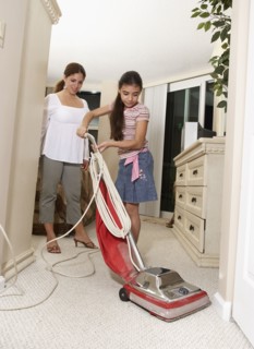Hispanic mother watching daughter vacuum