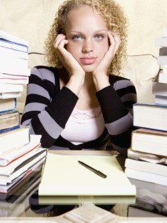 Young woman studying at desk with large stacks of books and notepad