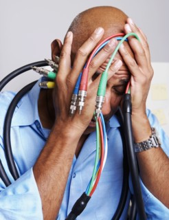 African businessman holding computer cables with head in hands