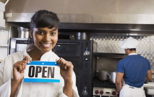 Mixed Race female chef holding Open sign in kitchen