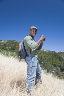 Mixed race man backpacking on hillside with binoculars