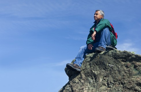 Mixed race man sitting on rocky hilltop