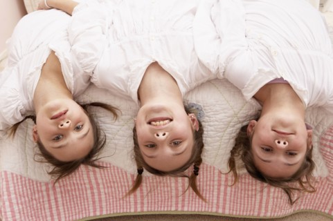 Mixed race girls hanging upside down from bed