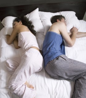 Couple sleeping back-to-back on bed
