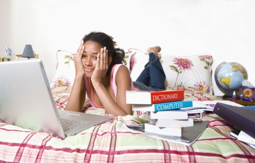Mixed race teenage girl doing homework on bed