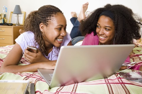 Mixed race teenage girls using laptop on bed