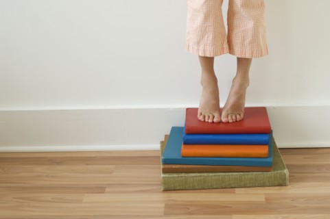 Girl standing on tiptoes on stack of books