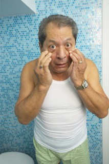 Hispanic man looking at his eyes in bathroom