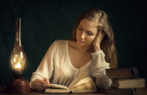Caucasian woman reading book by candlelight