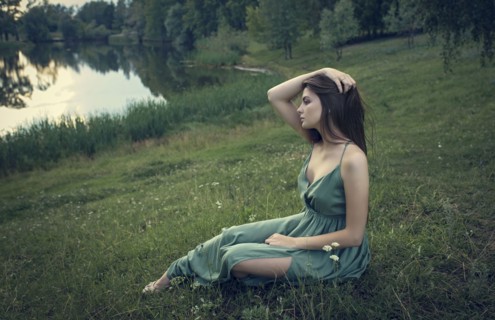Caucasian woman sitting in grass with wildflowers near lake