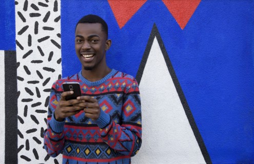 Black man using cell phone near colorful wall