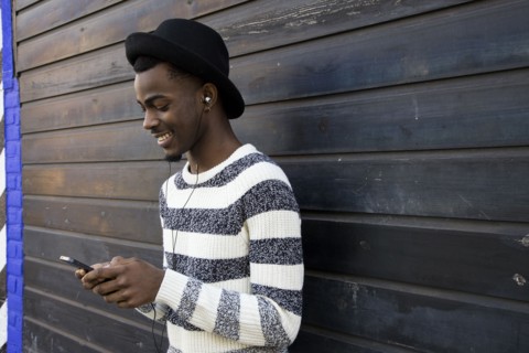 Black man listening to mp3 player near wooden wall