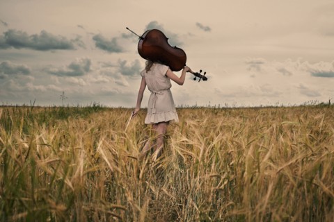 Caucasian girl carrying cello on shoulder in rural fieldCaption