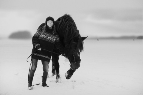 Caucasian teenage girl leading horse in snowy field