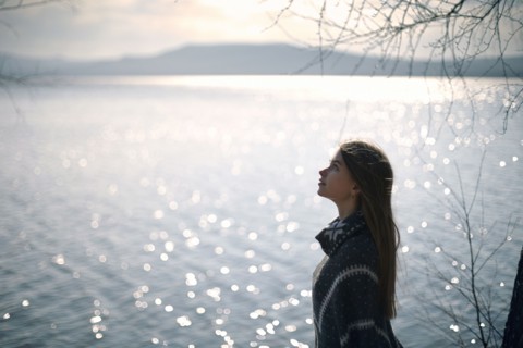 Pensive Caucasian girl at lake looking up