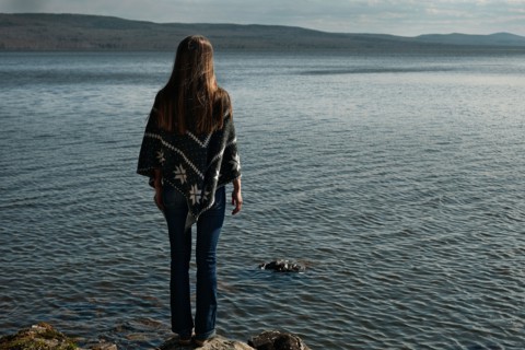 Pensive Caucasian girl standing on rock at lake