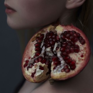 Caucasian girl balancing pomegranate slice on shoulder