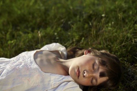 Caucasian girl laying in grass with eyes closed