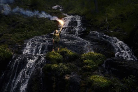 Caucasian girl holding smoke flare near waterfall