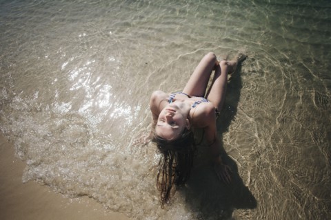 Caucasian woman wearing bikini sitting in waves on beach