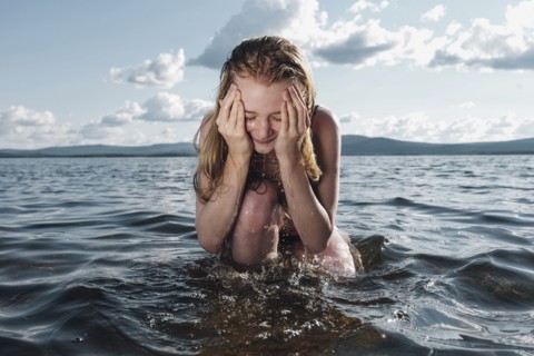 Caucasian teenage girl kneeling in ocean splashing water on face