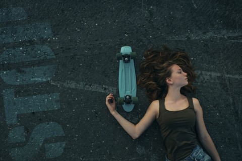 Caucasian teenage girl laying on pavement with skateboard