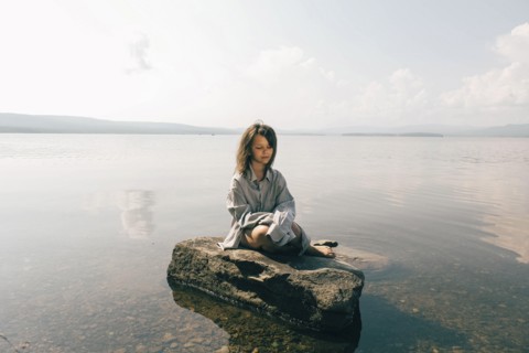 Caucasian girl sitting on rock in lake