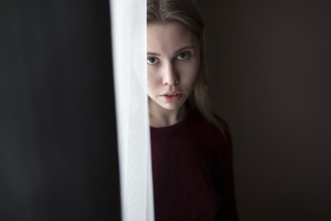 Serious Caucasian woman standing near curtain at window