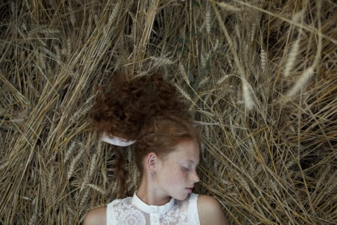 Serious Caucasian girl with freckles laying in wheat