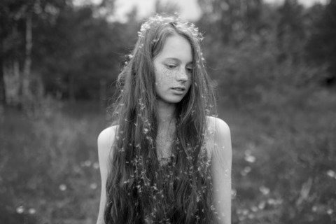 Caucasian girl standing in field with fuzz in hair