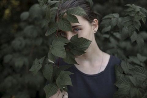 Face of Caucasian teenage girl behind leaves