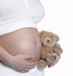 Caucasian woman holding teddy bear to pregnant belly