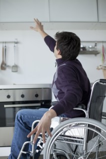 Caucasian man in wheelchair reaching for kitchen cabinet