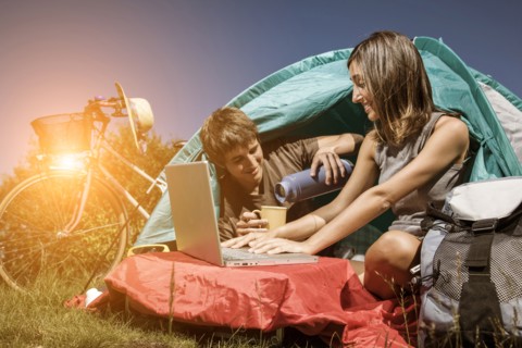 Couple drinking coffee and using laptop in camping tent