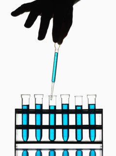Hand holding pipette dripping blue liquid into test tubes