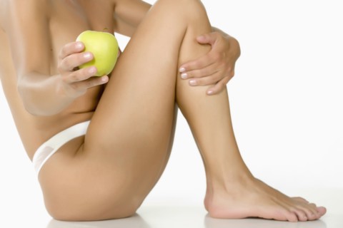 Caucasian woman sitting on floor showing green apple