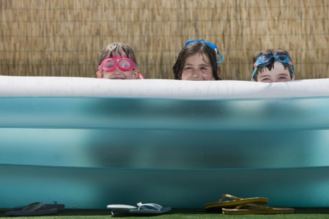 Smiling Caucasian children hiding in inflatable swimming pool