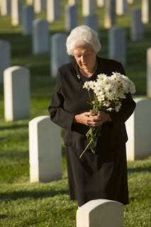 Caucasian widow holding bouquet at cemetery gravestone