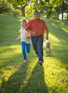 Hispanic brother and sister running with dog on hill