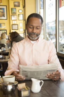 Mixed Race man reading newspaper in coffee shop